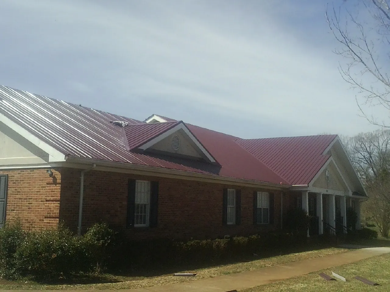 Red metal roof with gabled entries on a long brick building, from a Hail Damage Roof Repair job in Holton