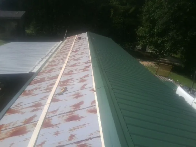 Old rusted panels beside newly installed green metal roofing — Wind Damage Roof Repair by Roofing Brothers in Holton