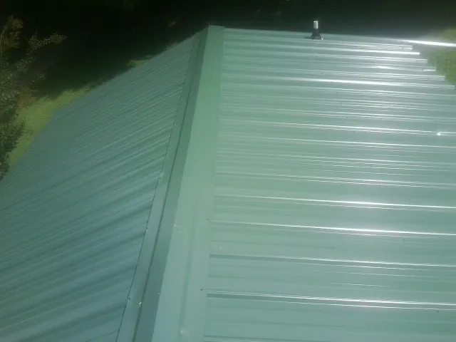 New green metal panels meeting at the ridge of a roof — Flat Roof Repair work by our crew in Holton