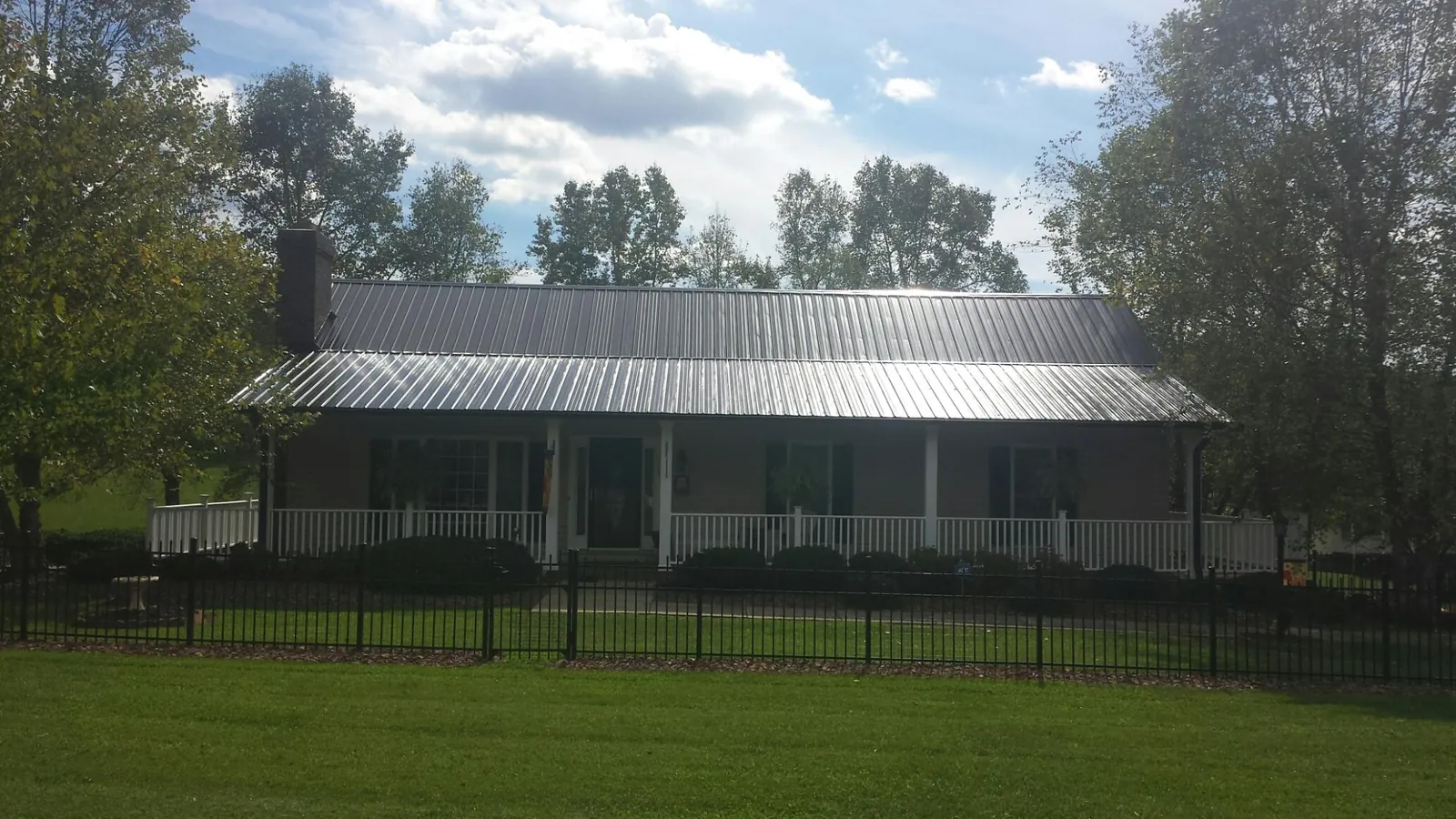 Gray metal roof on a brick ranch with a full width front porch — Gutter Guard Installation work by our crew in Holton