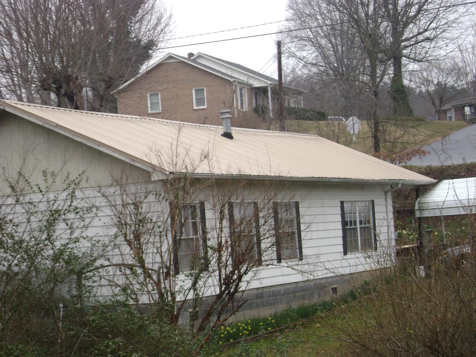 Tan metal roof on a white sided house set into a hillside — Commercial Roofing by Roofing Brothers in Holton