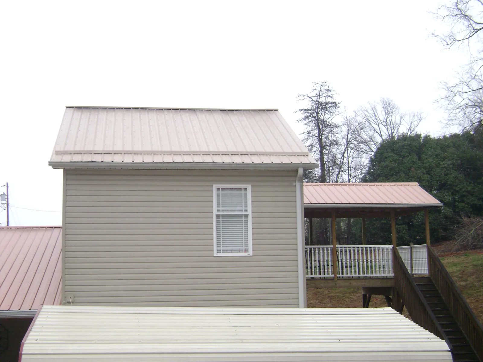 Tan metal roofs on a two story addition and attached porch, from a Roof Replacement job in Holton